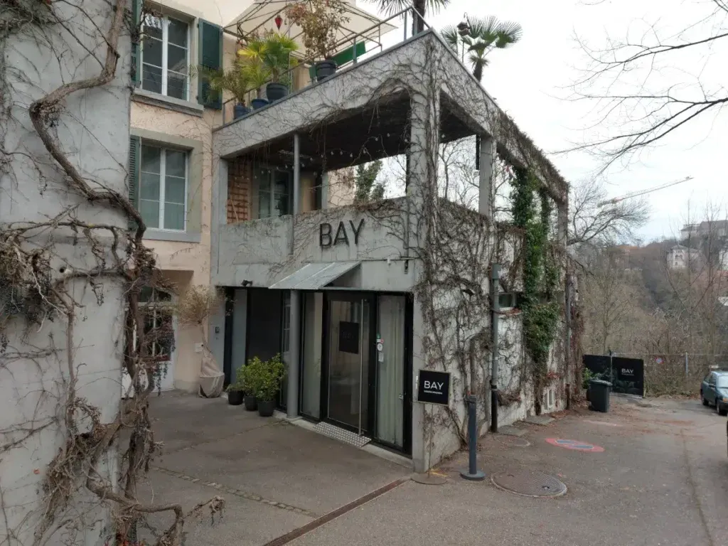 Eingangsbereich des Restaurants Bay Bern von aussen in einem modernen Betongebäude, das grossflächig mit Kletterpflanzen bewachsen ist