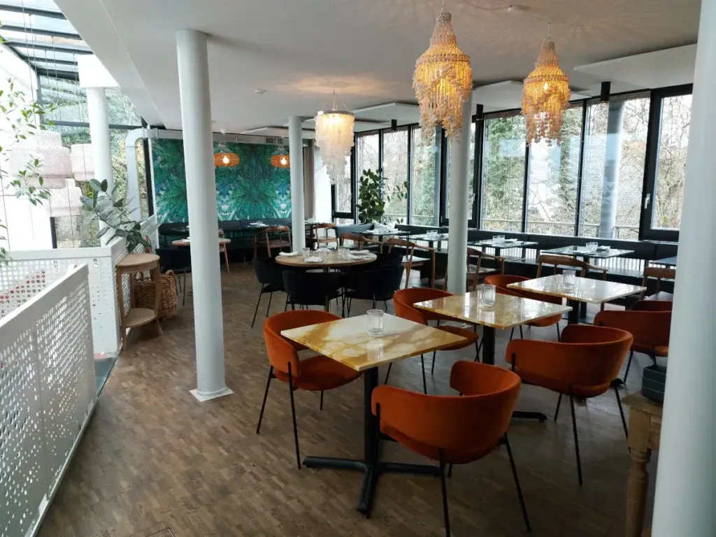 Blick in den hellen Gastraum des Restaurants Bay Bern mit weissen Säulen, orangefarbenen Polsterstühlen und grossen Panoramafenstern