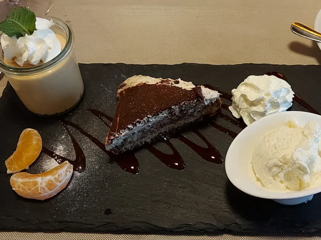 Café Gourmand at Ratskeller Bern: Dessert selection with caramel cream, Christmas tiramisu, and vanilla ice cream on a slate plate.