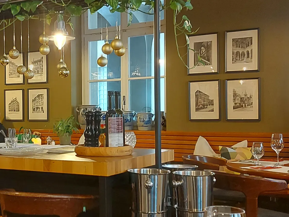 Elegant interior of Ratskeller Bern: Olive-green walls, photos of Bern's Old Town, and stylishly set tables.