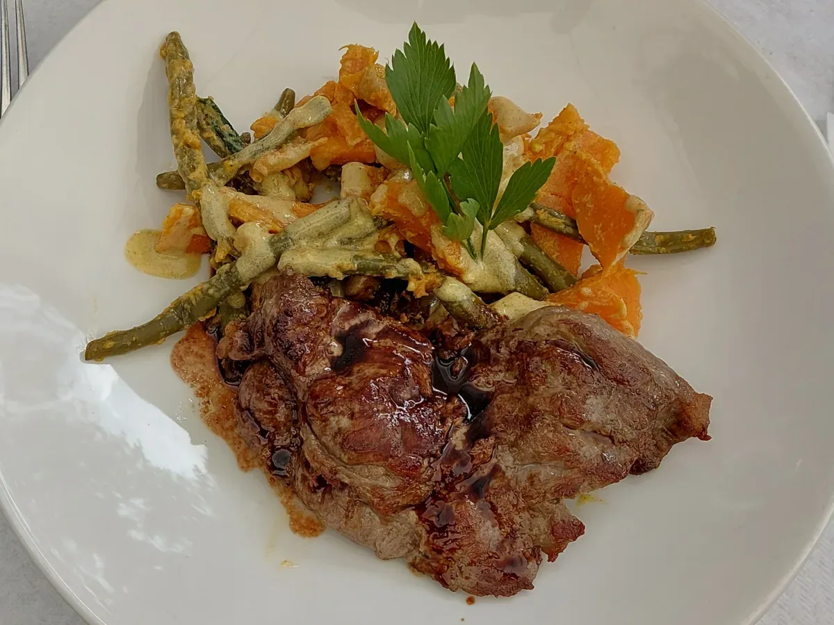Spider steak with brown jus, sweet potato salad with green beans and creamy dressing on a white plate
